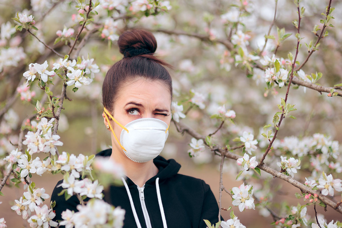 Une jeune femme allergique masquée ,sous un arbre fruitier, se protège des pollens