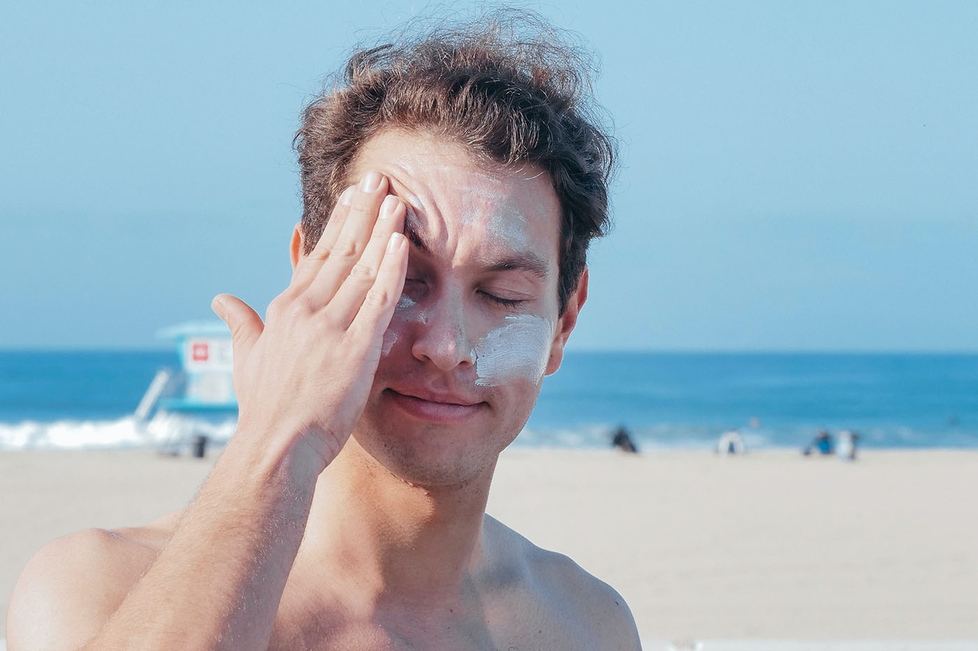 un vacancier sur une plage s'étale de la crème solaire sur le visage
